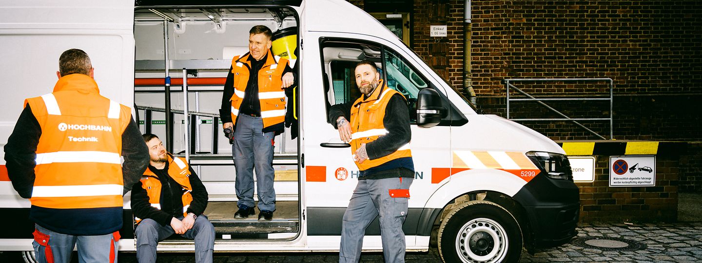 Handwerker der HOCHBAHN sitzen in und vor einem Dienstfahrzeug